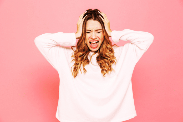 stressed woman holding her head in her hands on a capri pink background